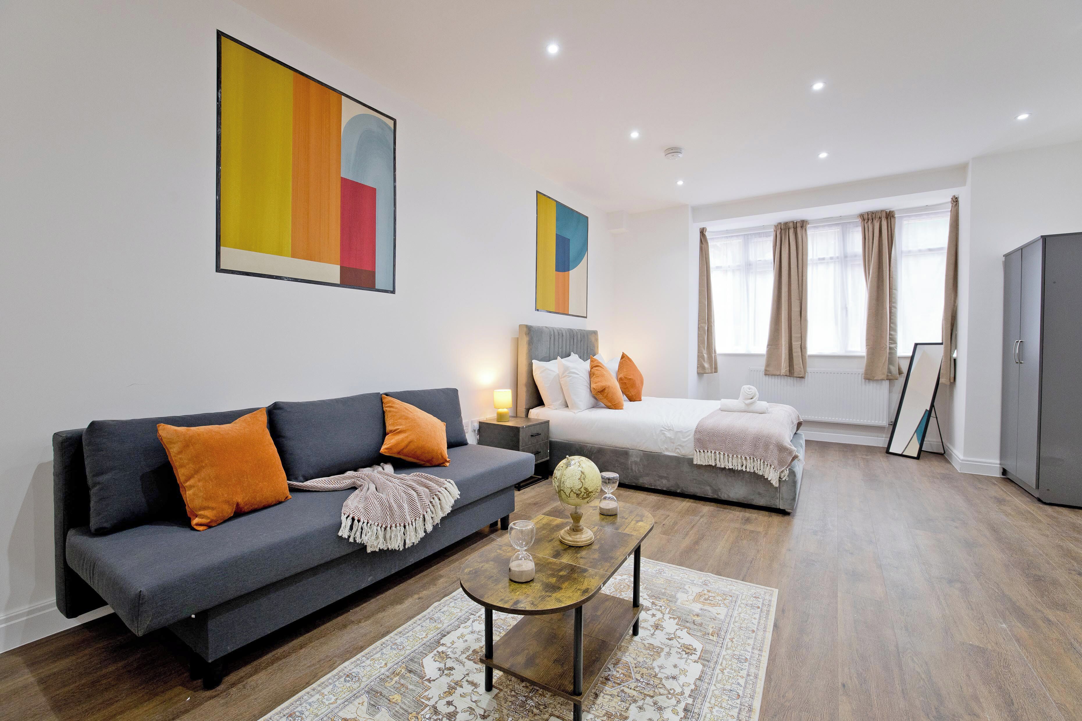 Ein modernes Hotelzimmer mit grauem Sofa, einem weißen Bett, einem Holztisch und abstrakter Kunst an den Wänden.