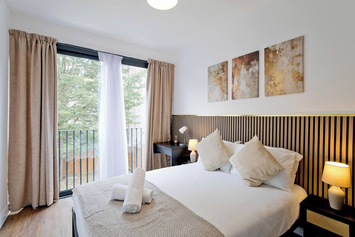 Une chambre d’hôtel avec un grand lit, deux lampes de chevet, une vue sur l’extérieur et trois œuvres d’art abstraites accrochées au mur.