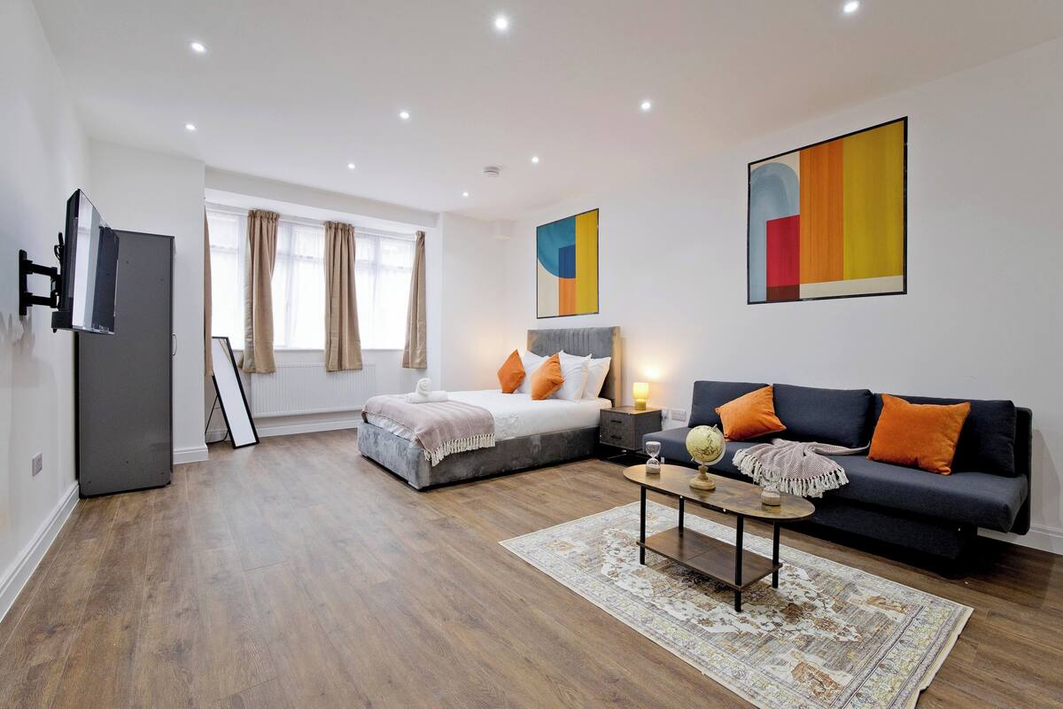 Une chambre moderne avec un lit, un canapé, une télévision et des œuvres d’art accrochées aux murs.