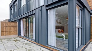 Een modern gebouw met grote schuiframen, een houten omheining en een verhard terras.