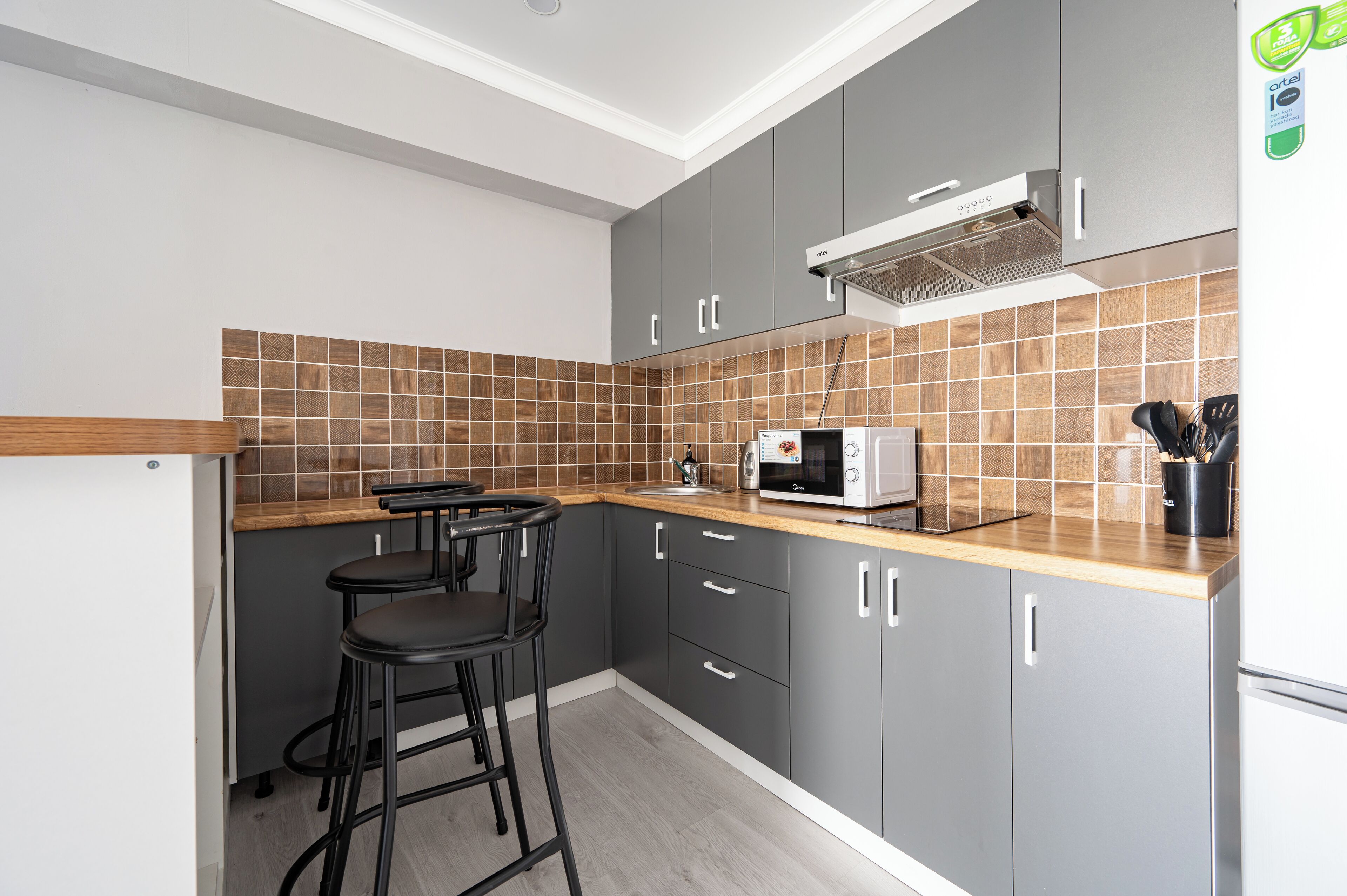 A modern kitchen with grey cabinets, a wooden countertop, a microwave, and two black bar stools.