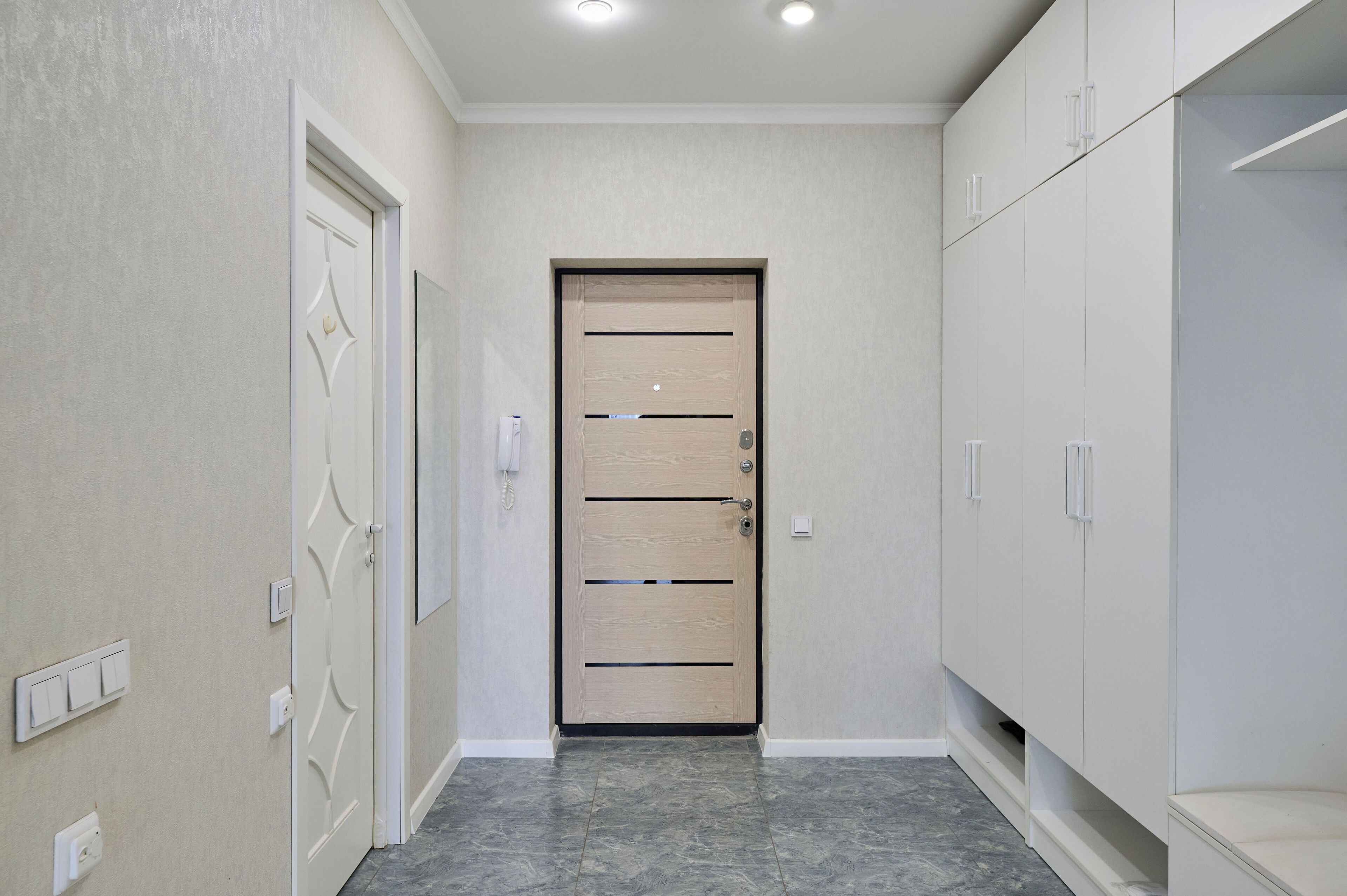 A hallway with a modern door, white walls, and a tiled floor.