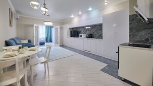 Una cocina moderna con armarios blancos, salpicadero de mármol y un comedor con mesa y sillas blancas.