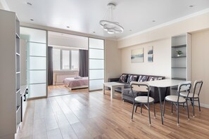 Una sala de estar moderna con sofá, mesa de centro y sillas. Hay un ventanal corredero que da a un dormitorio.