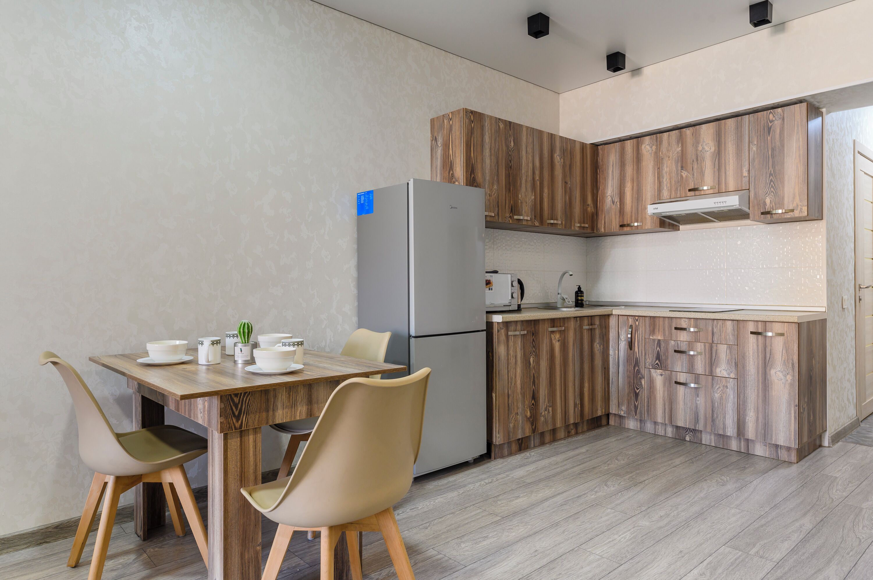 A modern kitchen with wooden cabinets, a built-in refrigerator, and a dining area with two chairs and a table.