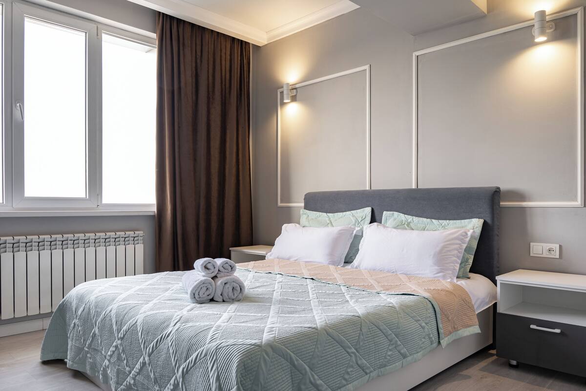 A modern bedroom with a large bed, a bedside table, a nightstand, and a window with curtains.