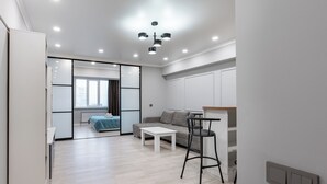 Una sala moderna con sofá, una mesa de centro y un comedor con una silla. Hay una puerta corrediza que da a otra habitación.