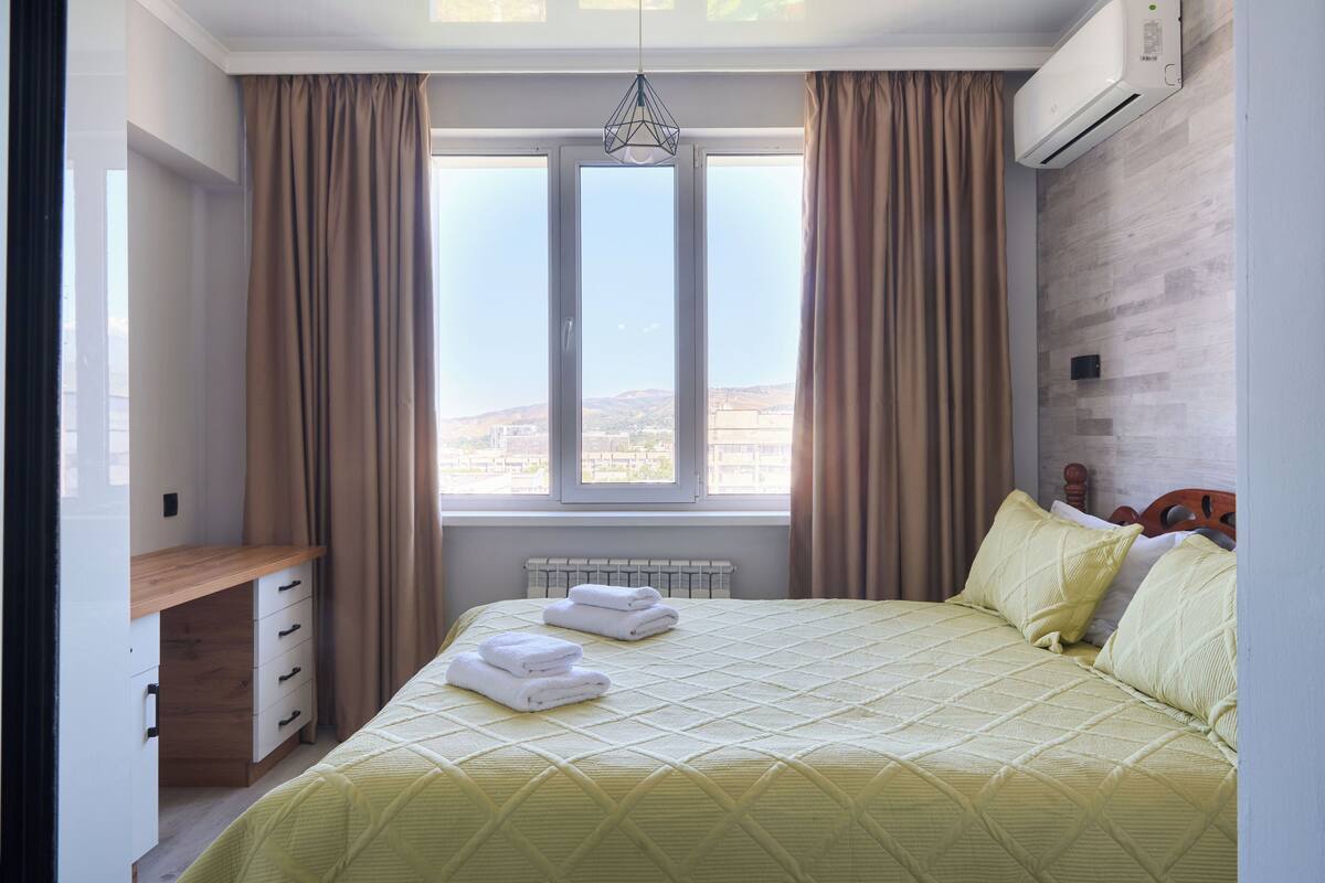 A bedroom with a bed, a desk, and a window with curtains.