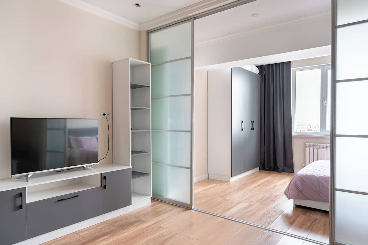 A modern bedroom with a TV, sliding closet doors, a bed, and a large window.