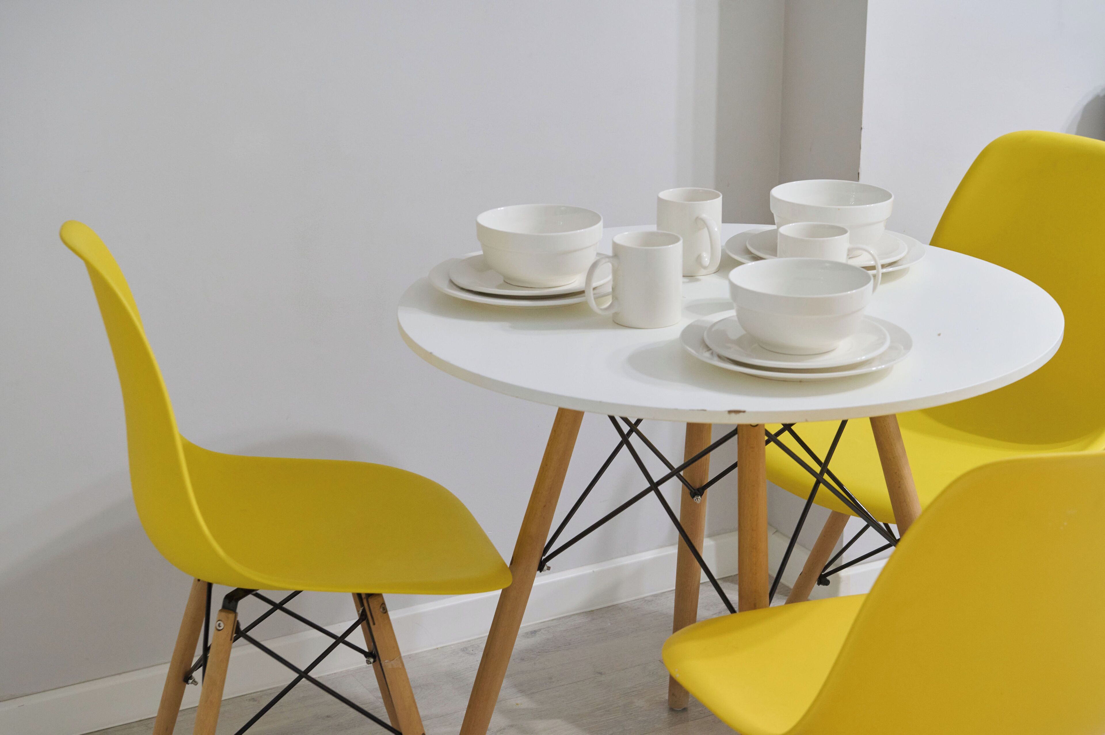 A round white table with four yellow chairs, white cups, and saucers.