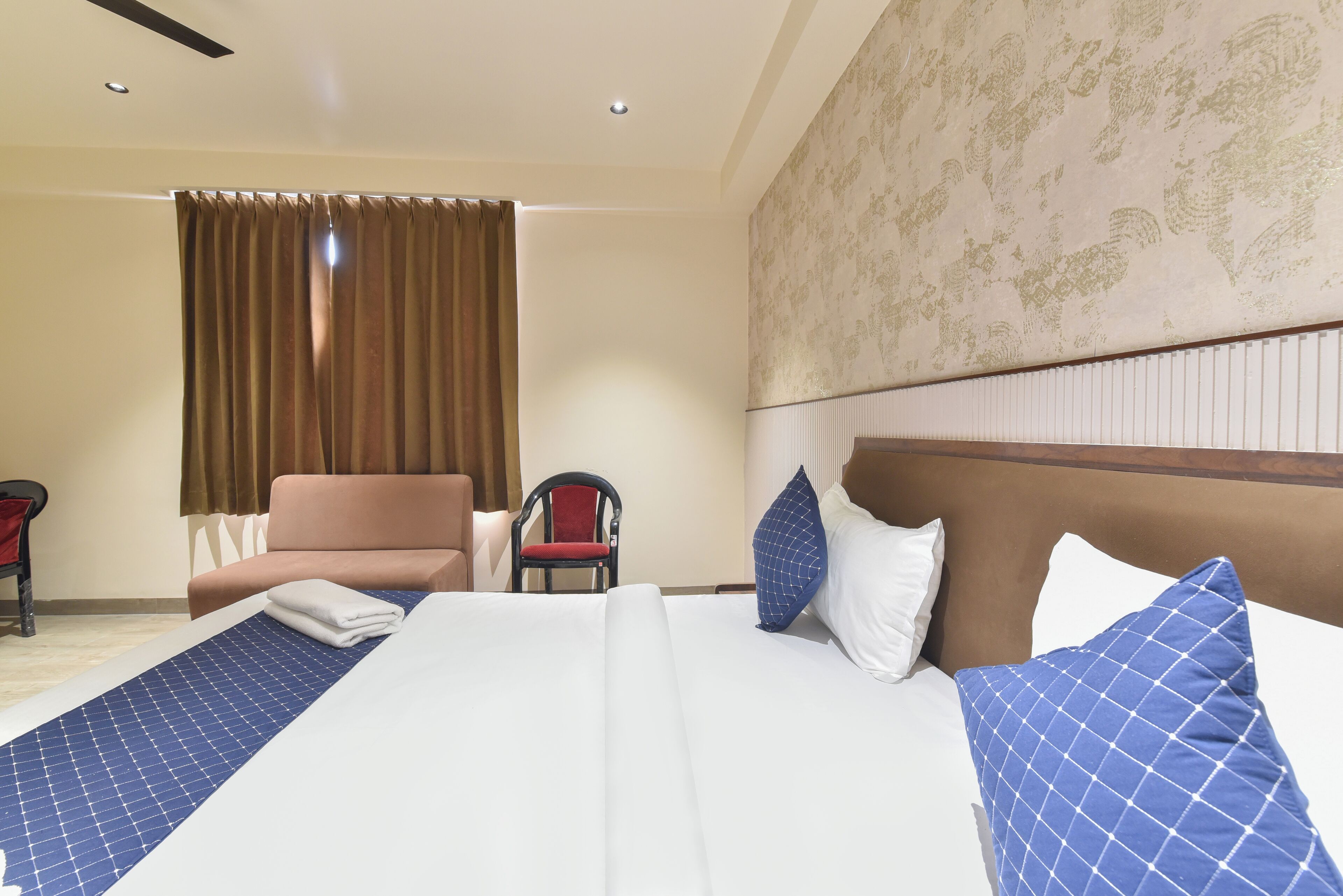 A hotel room with a large bed, a chair, a desk, and a window with curtains.