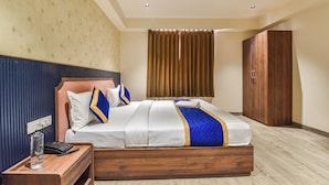 A hotel room with a wooden bed, a nightstand with a bottle and phone, a wardrobe, and a curtain. - Stay Casa Inn (Jaipur)