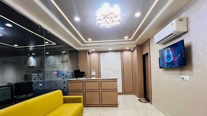 A modern living room with a yellow sofa, a kitchen area with a built-in island, and a mounted TV. - Stay Casa Inn (Jaipur)