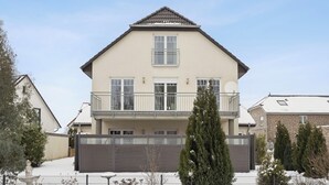 Une maison à deux étages avec un balcon, une allée fermée par un portail et un toit recouvert de neige.