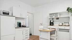 Une cuisine moderne avec des meubles blancs, un four à micro-ondes, une machine à café et une table à manger en bois avec des chaises.