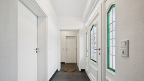 Un couloir aux murs blancs, au sol foncé et à la fenêtre encadrée de vert.