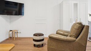 Un salon moderne avec un canapé en cuir, un tabouret en bois et un téléviseur fixé au mur.