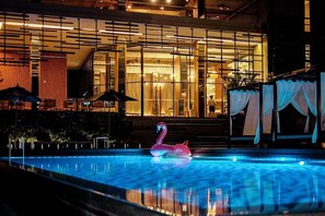 A swimming pool with a pink flamingo float, a covered seating area, and a building with large windows and a brick facade. - Brique Suite Hotel Chiangmai (Chiang Mai)
