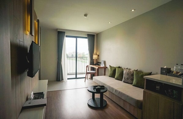 A modern hotel room with a sofa, a small table, a TV mounted on the wall, a desk with a chair, and a balcony with curtains. - Brique Suite Hotel Chiangmai (Chiang Mai)