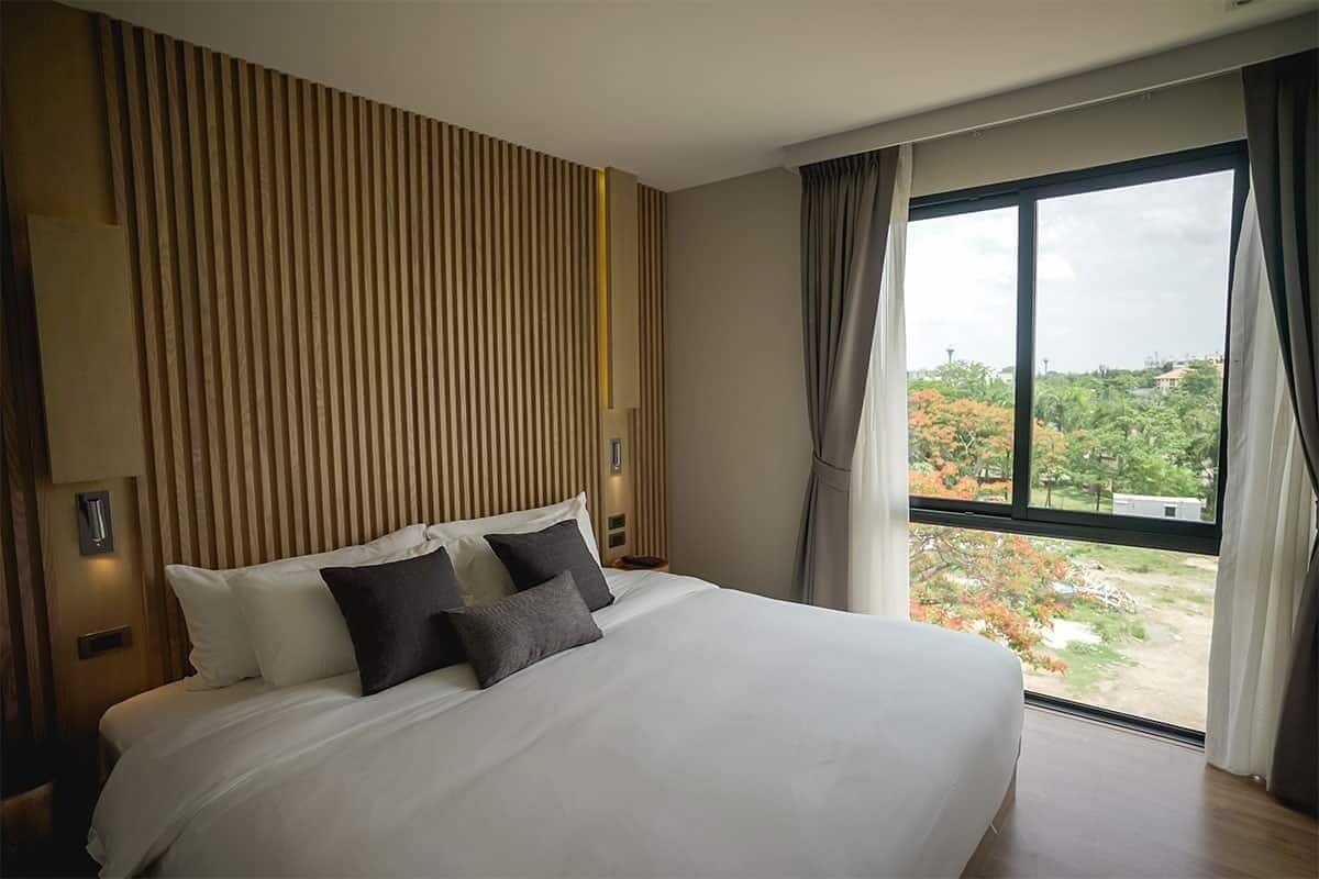 Une chambre d’hôtel moderne avec un grand lit, une vue sur les arbres par la fenêtre et un mur revêtu de panneaux en bois.