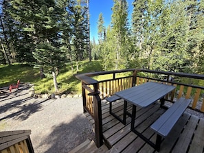 Une terrasse en bois, agrémentée de tables de pique-nique et de bancs, entourée d’une zone boisée.