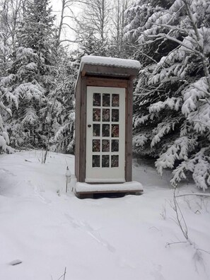 A wooden structure with a door and windows, surrounded by snow-covered trees.