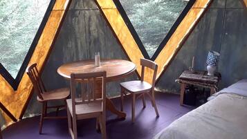 Quarto com mesa de madeira e cadeiras, um criado-mudo com abajur e uma cama.