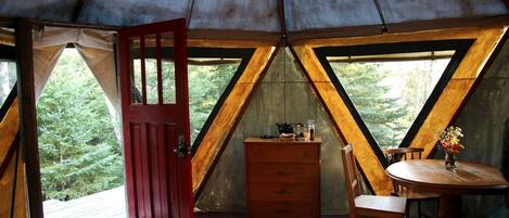 Een tent met houten binnenkant, een rode deur, een tafel met stoelen en een dressoir.