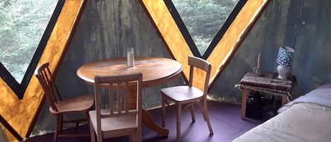 Una habitación con una mesa de madera y sillas, una mesita de noche con lámpara, y una cama.