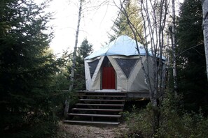 A forested area with a tent-like structure featuring a red door and steps leading up to it.