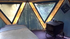 Une pièce triangulaire comprenant un lit, une petite table et une fenêtre.