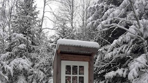 A wooden structure with a door and windows, surrounded by snow-covered trees.