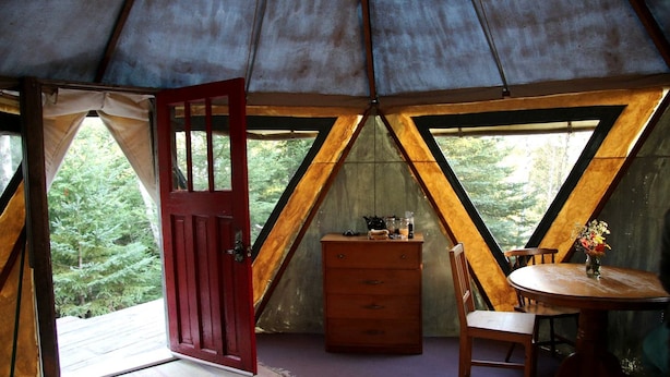 A tent with a wooden interior, a red door, a table with chairs, and a dresser.