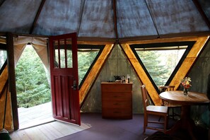 A tent with a wooden interior, a red door, a table with chairs, and a dresser. - Yurt Nestled in Nature on Community in Nova Scotia, Canada (Maple Grove)
