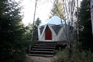 A forested area with a tent-like structure featuring a red door and steps leading up to it.
