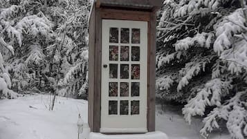 A wooden structure with a door and windows, surrounded by snow-covered trees.
