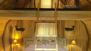 Une chambre dans un chalet en bois, avec un lit, deux lampes fixées au mur et une fenêtre avec des rideaux.