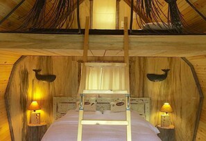 Een slaapkamer in een houten blokhut met een bed, twee wandlampen en een raam met gordijnen.