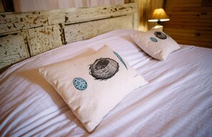 A bed with two pillows featuring a bird's nest design, a wooden headboard, and a bedside lamp. - Luxurious Woodland Cabin in Nova Scotia (Baddeck)