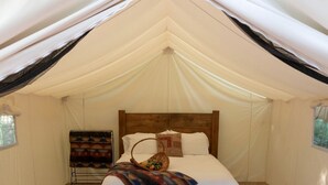 A tented room with a bed, a blanket, and a basket.