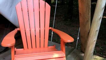 A wooden deck with a single orange Adirondack chair.