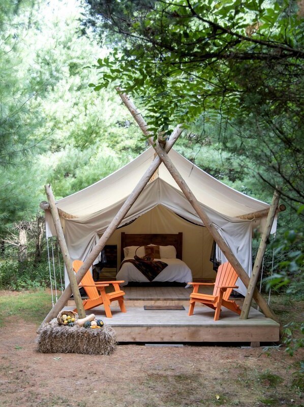 A tent with a bed, two chairs, and a hay bale with vegetables.