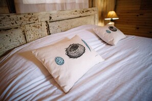 A bed with two pillows featuring a bird's nest design, a lamp, and a rustic wooden headboard.