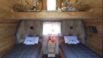 Une chambre mansardée chaleureuse avec deux lits, une petite fenêtre et un élément décoratif en métal placé au-dessus des lits.