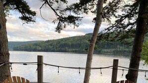 Una mesa al aire libre con mantel a cuadros, platos, vasos y botellas, rodeada de sillas de madera.