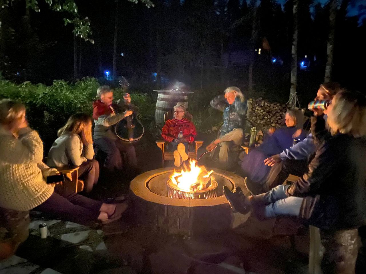 Eine Gruppe von Menschen sitzt um eine runde Feuerstelle in einer Außenanlage.