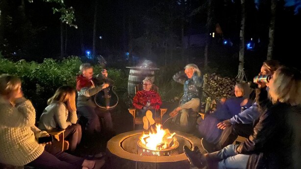 A group of people seated around a circular fire pit in an outdoor setting. - Cardinal's Inn Cabin Rental in Nova Scotia (Baddeck)