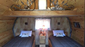 A cozy attic bedroom with two beds, a small window, and a decorative metal piece above the beds.