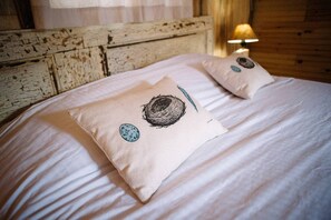 A bed with two pillows featuring a bird's nest design, a lamp, and a rustic wooden headboard. - Cardinal's Inn Cabin Rental in Nova Scotia (Baddeck)