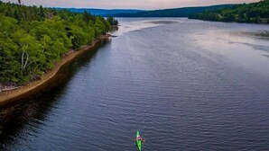 A kayaker on a calm river surrounded by dense forest and distant hills. - Cardinal's Inn Cabin Rental in Nova Scotia (Baddeck)
